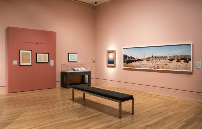 an art gallery with a panoramic photo of boys running with wind turbines in the back