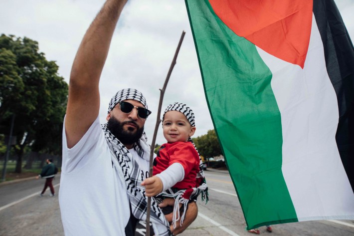 A man holds a young child in one hand and a flag in the other.