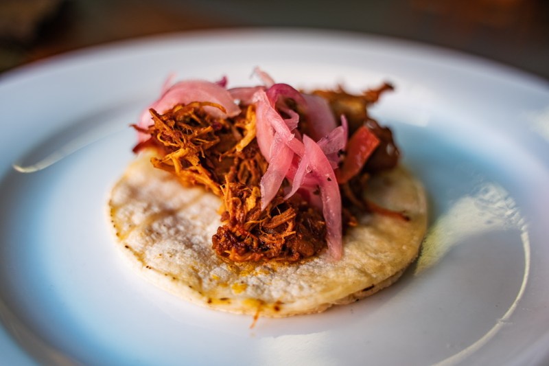 A Cochinita Pibli taco garnished with red pickled onions