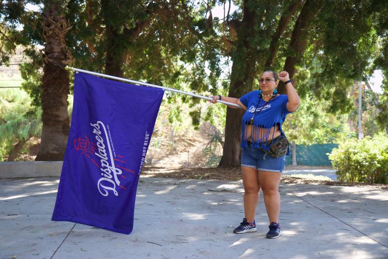 Melissa Arechiga founder of Buried Under the Blue a website and group made up of families and descents of families who were displaced better known as the removal of Chavez Ravine stands holding a "Displacers" flag. Photo by Janette Villafana for L.A. TACO.