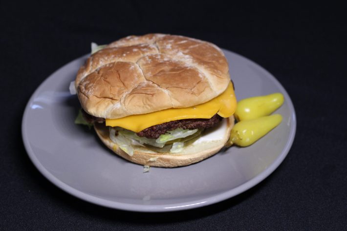 Double cheeseburger on a plate next to a couple of hot peppers.