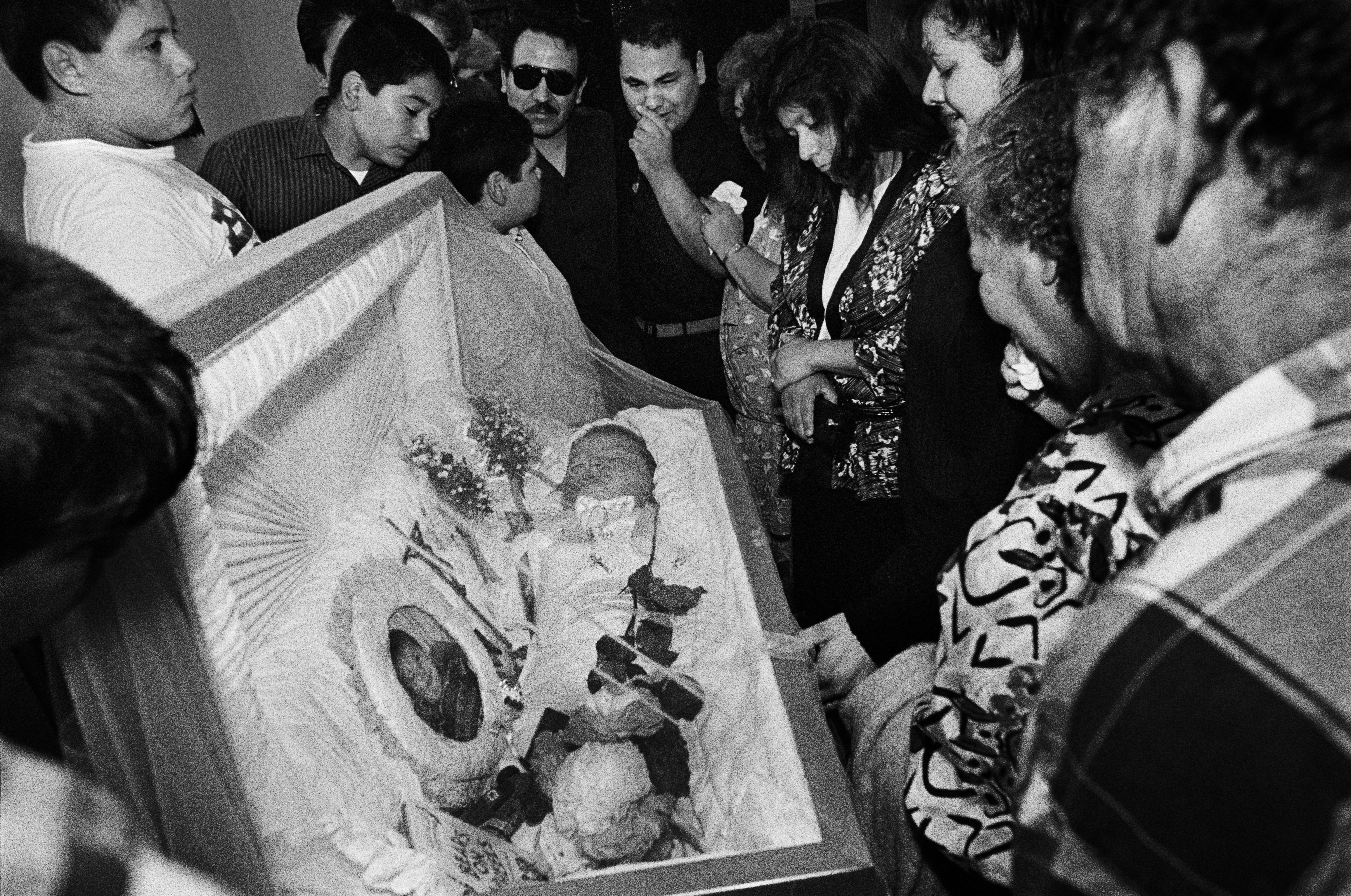 A family gathers the round of the coffin of Thomas Regalado III, who was killed by a stray bullet during a drive-by shooting. East Los Angeles, CA 1992