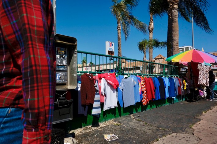 A row of t-shirts put on display by a street vendor hangs along the fence of a shopping center on 8th Street and Vermont Avenue in Koreatown, Los Angeles, California. (March 2022).