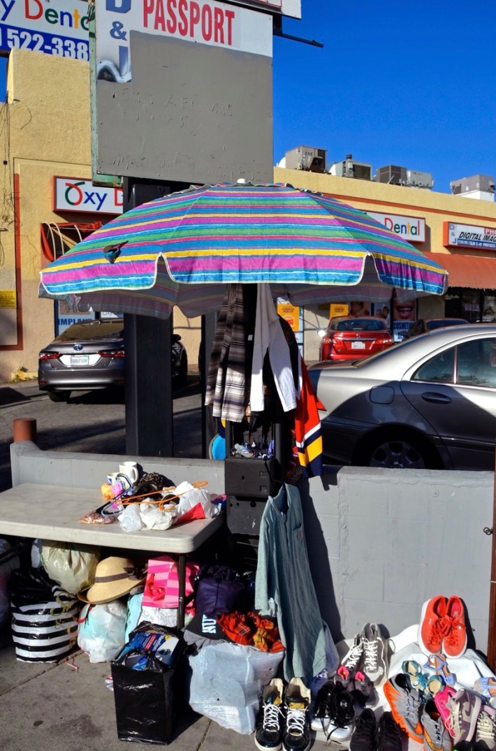 A street vendor’s umbrella and merchandise shades the remains of what’s left of a Payphone on the corner of Vermont Avenue and Burns Avenue in East Hollywood, Los Angeles, CA. Aug. 10, 2021.