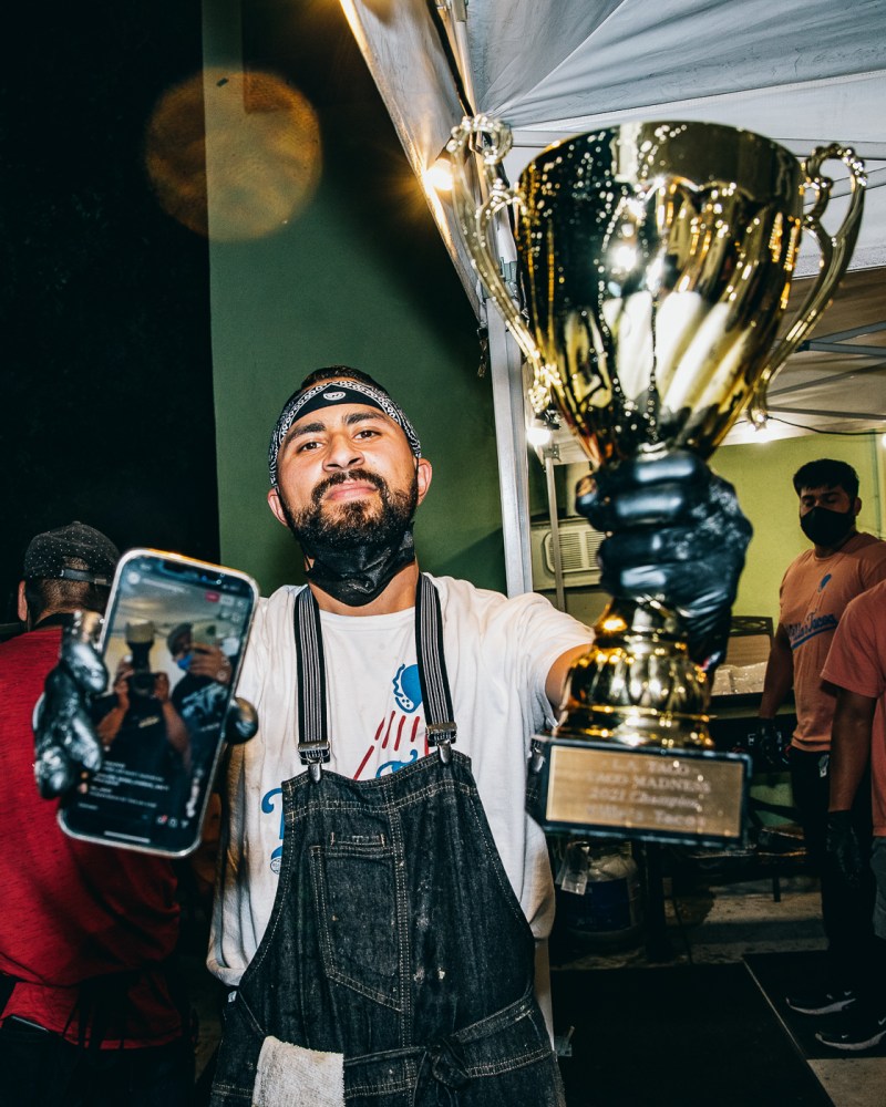 Vic Villa holds up a phone and the 2021 TACO MADNESS trophy