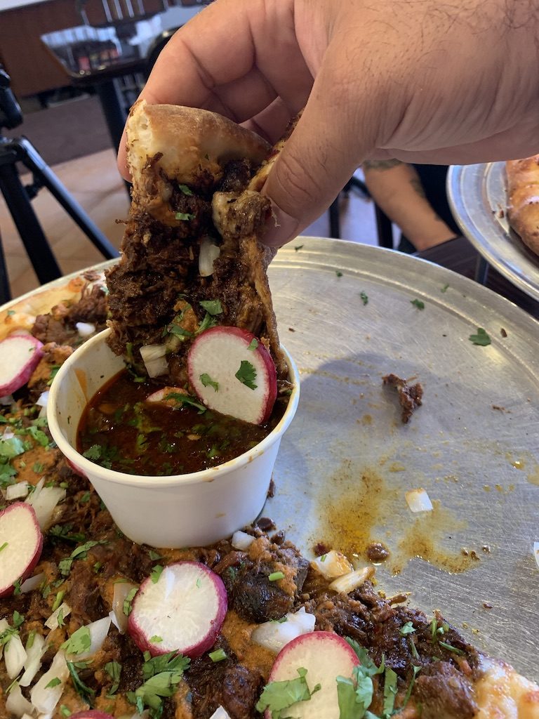 Dunking a slice of birria pizza into consomé at Rose City Pizza. Photo from the L.A. TACO archives.