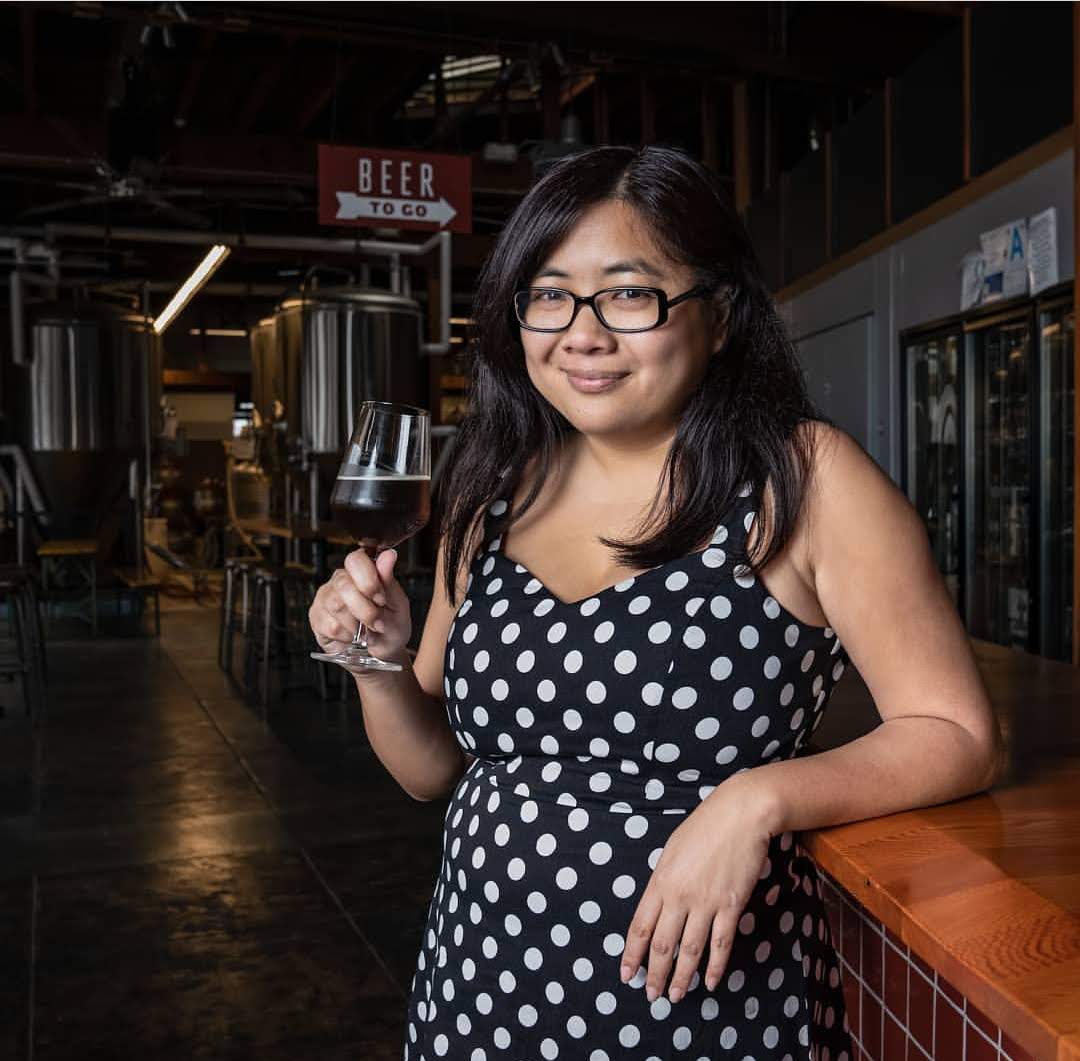 A woman holding a glass of beer in a brewery