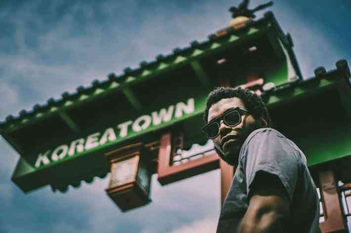 Rapper the Koreatown Oddity poses in front of a sign reading "Koreatown"