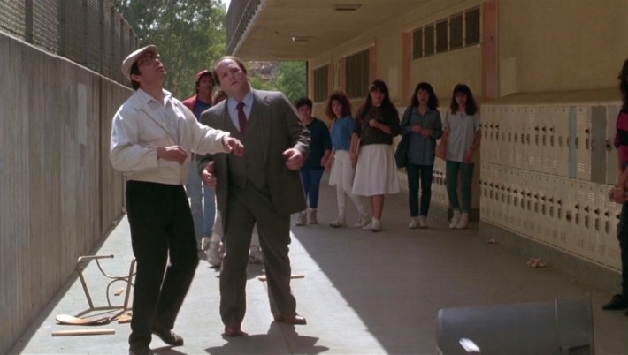 Mr. Escalante looks up as a trash can and desk chair are thrown over a balcony. Photo via Warner Bros. Pictures.